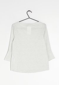 Helles graues Langarmoberteil mit rundem Ausschnitt und ausgestellten Ärmeln. Weiche Textur, hängt an einem schwarzen Metallhaken, Rückansicht angezeigt.