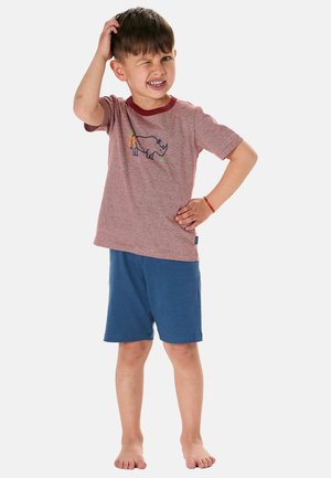 Young boy standing barefoot with one hand on hip and the other scratching his head, wearing a rhino print t-shirt and blue shorts.