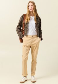 Lepardmönstrad jacka, vit t-shirt, beige byxor och vita sneakers med bruna detaljer. Modellen bär en brun axelväska.