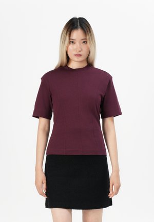 Burgundy short-sleeve top with a round neckline, featuring a fitted design and seam detailing; paired with a black textured mini skirt.