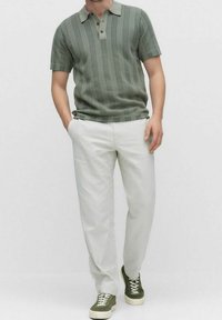 Grönrandig pikétröja med en beige krage, kombinerad med vita byxor och olivgröna sneakers, med texturerad tyg och avslappnad passform.
