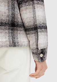 Ruudullinen paita beige, musta ja valkoinen sävyissä; valmistettu teksturoidusta kankaasta, jossa on napitettu hihansuu ja suora helma.