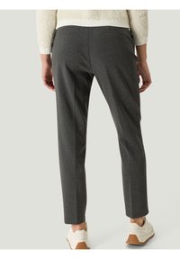 Szare dopasowane spodnie o gładkiej fakturze, z wąskim krojem i tylnymi kieszeniami, zestawione z jasnymi trampkami.