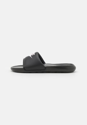 Black slide sandal with a textured sole, wide straps, and a logo. Made from synthetic material, featuring a minimalist design.