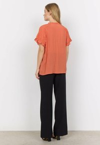 Rust-colored top with textured fabric and ruffled sleeves, paired with black wide-leg trousers. Simple design with a relaxed fit.