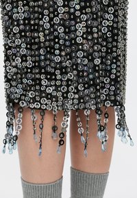Črno krilo z bleščicami s krožnimi bleščicami, kovinskimi poudarki in visečimi kroglicami z modrimi kapljicami na robu. Mehka tekstura tkanine.