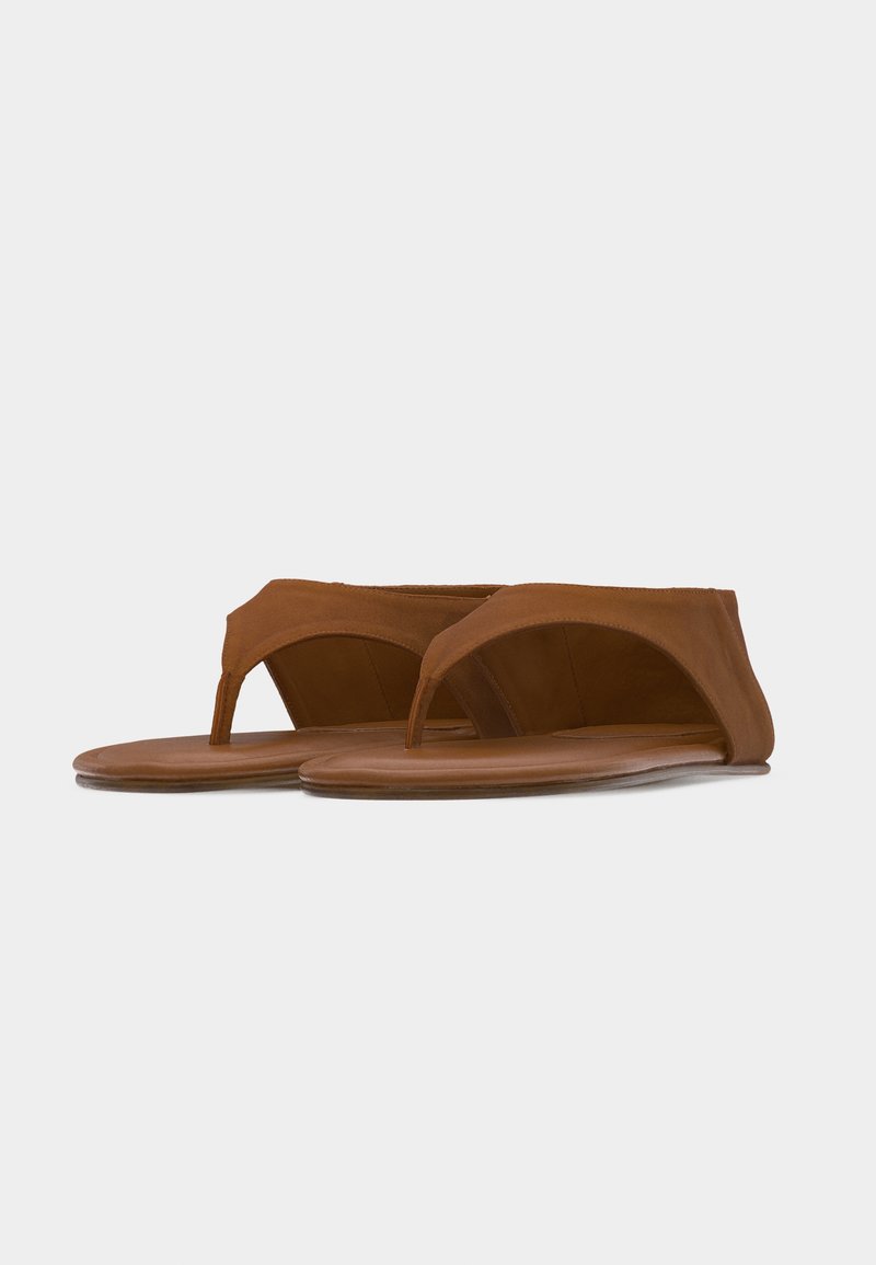 Sandales plates en cuir marron avec larges brides sur les orteils et un design minimaliste sur fond blanc.