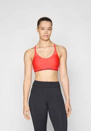 Red sports bra with a V-shaped design, thin adjustable straps, and a black elastic band featuring "ARMOUR" logo at the bottom.