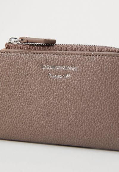 Brown textured leather wallet featuring a silver logo, zip closure, and smooth hardware accents. Dimensions not specified.