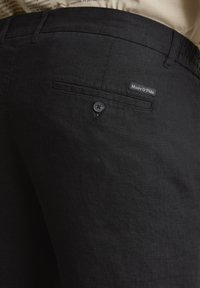 Zwarte linnen broek met een achterzak met een knoop en een klein geweven label met de tekst "Marc O'Polo." Geweven stof met een subtiele glans.