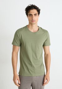 T-shirt en coton vert olive avec un col rond et des manches courtes, présentant un petit logo sur la poitrine. Texture lisse, design ajusté.