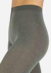 Legginsy w ciemnooliwkowym kolorze, wykonane z miękkiego, elastycznego materiału. Posiadają prosty design z żebrowanym pasem w talii i gładką teksturą.