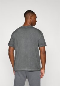 Camiseta de algodón gris con cuello redondo y mangas cortas, con una textura suave y un dobladillo recto. La vista trasera muestra un diseño liso sin patrones.