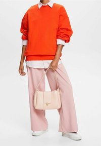 Sudadera naranja de gran tamaño, camisa blanca con cuello debajo, pantalones rosa de pierna ancha, sosteniendo un bolso rosa claro con detalles de hardware.