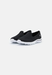Black slip-on shoes with a textured upper, elasticated sides, and a white rubber sole featuring subtle black accents. Lightweight and breathable design.