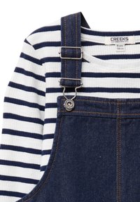 Salopette di denim blu navy con spalline regolabili, hardware argentato e una maglietta bianca a maniche lunghe con righe orizzontali blu navy.