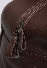 Brown leather bag with a zipper closure, featuring sturdy metal hardware and contrasting stitching details along the seam.