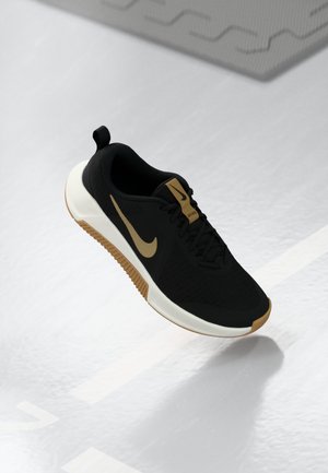 Schwarzer und goldener Nike Laufschuh mit weißer Sohle, schwebend in der Luft auf einem hellgrauen Sportplatz mit Spielfeldlinien.
