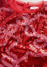 Abito rosso in paillettes con superficie testurizzata. Presenta motivi ondulati in paillettes rosa più chiare. Fodera in tessuto morbido con chiusura a bottone.