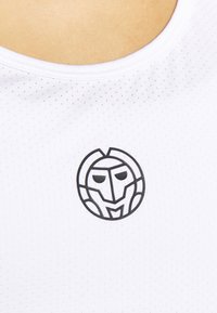 Vit prestationsskjorta med en slät struktur, med en svart geometrisk logotyp i mitten och en rundad halsringning.