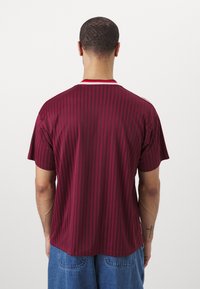 Maglietta a maniche corte a righe marrone con colletto rosso e bianco, realizzata in tessuto leggero. Presenta righe di accento laterali e una vestibilità comoda.