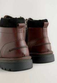 Braune Leder-Stiefel mit einem schwarzen Textilkragen, seitlichem Reißverschluss und strukturiertem schwarzen Gummisohle. Mit gestickten Akzenten und abgerundeter Zehenpartie.