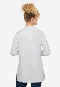 Camicia bianca a maniche lunghe con taglio dritto, spalla a yoke e spacchi laterali. Tessuto di cotone liscio con cuciture minime e senza motivi.