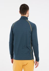 Tamsiai mėlynas, ilgomis rankovėmis polarinis marškinėliai su aukštu apykakle, papuošti kontrastinga auksine siūleliais ant pečių ir rankovių.