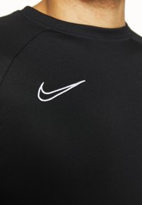 Camiseta deportiva negra hecha de un tejido suave y ligero con cuello redondo, que presenta un logo de Nike en blanco en el pecho.