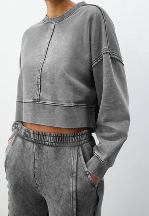 Personne portant un sweat-shirt court gris et un pantalon de survêtement gris assorti avec une taille élastique et les mains dans les poches.