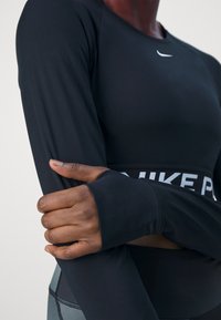 Urheilija, jolla on päällään musta pitkähihaisuus treenitoppi, jossa on peukalon reikä, ristittäessä kädet, ja näkyy Nike-logo rinnassa ja vyötärönauhalla.