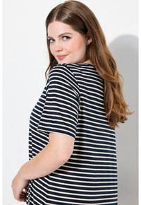 Camiseta de rayas en azul marino y crema con mangas cortas, cuello redondo y un corte relajado. La tela suave se ajusta suavemente sobre el cuerpo.
