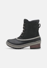 Botín impermeable negro hasta el tobillo con parte inferior de goma, acentos grises, cinco ojales metálicos y un cuello de tejido gris texturizado. Tacón robusto de madera.