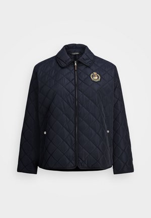 Veste matelassée navy avec zip sur le devant, col, poches latérales et un blason brodé. Le tissu semble lisse et léger.