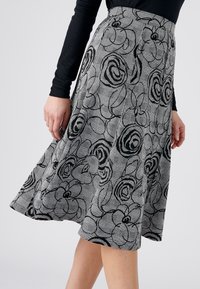 Een zwart-wit rok met bloemmotief, in een flared vorm en gemaakt van gestructureerde stof, met een hoge tailleband en een knielange stijl.