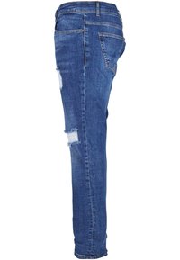 Modri denim kavbojki s oprijetim krojem, ki imajo obrabljene kolenske obliže, raztrgane robove in standardne zadnje žepke.