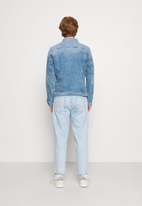 Ljusblå denimjacka med klassisk passform, med två fickor och kontrasterande sömmar. Bärs över ljusblå jeans och sneakers.