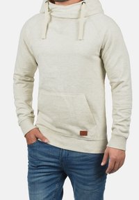 Jasno-beżowy hoodie z miękkiego materiału, z kapturem, sznurkami do regulacji i przednią kieszenią. Zawiera małą skórzaną naszywkę z brązowym logo.