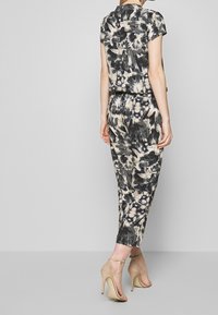 Jumpsuit senza maniche a palloncino in tonalità di nero e crema; presenta una vestibilità rilassata e lunghezza ankle, abbinato a sandali con tacco nudo.