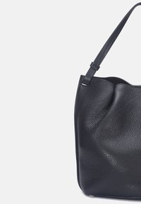 Sac à main en cuir noir avec une surface texturée, doté d'une seule bandoulière et d'un design à ouverture supérieure. Courbes subtiles aux bords.
