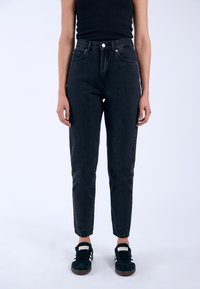 Högmidjade svarta denimjeans med rak passform, femficksdesign och synliga sömmar, kombinerade med svarta sneakers.