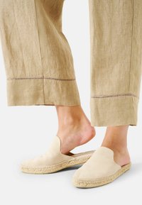 Beige mockaskor med rund tå och vävd jutesula, tillsammans med lösa linnbyxor med en detaljerad fåll.