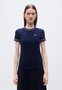 Μπλε ναυτικό βαμβακερό T-shirt με κοντά μανίκια, λευκή γιακά και περιμετρικό τελείωμα στα μανίκια, με μικρό πράσινο κεντητό λογότυπο στο στήθος.