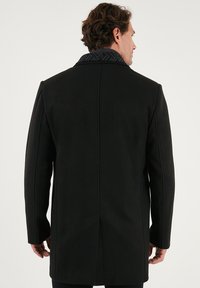 Abrigo negro con corte entallado y cuello con estampado. Cuenta con hombros estructurados y una abertura trasera para mayor movilidad.