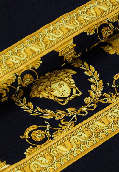 Mustan kankaan pinnassa on monimutkaisia keltaisia barokkikuvioita, mukaan lukien Medusa-pää ja koristeellisia yksityiskohtia, joiden tekstuuri on sileä.