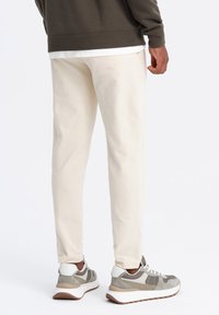 Crème-kleurige tapered sweatpants met zijzakken, gecombineerd met grijs-witte sport sneakers met een gestructureerde afwerking en rubberen zolen.