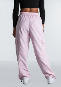 Lichtroze cargobroek met een elastische tailleband, zijzakken en een losse pasvorm. Het materiaal lijkt glad met een iets glanzende afwerking.