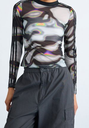 Person iført en langærmet mesh-top med sort, gråt og hvidt camouflage-mønster og sorte striber på ærmerne samt sorte cargobukser.