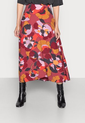 Falda larga con estampado floral que presenta flores rojas, amarillas y moradas sobre un fondo marrón granate. Combinada con botines de tacón negros.