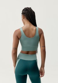 Un sujetador deportivo y leggings de cintura alta en un color azul verdoso apagado, con una textura suave y paneles en contraste. El diseño tiene un corte tipo racerback.